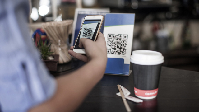 Person standing in front of a table scanning a qr code on his mobile phone.